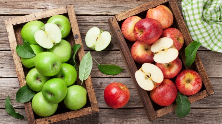 Auf einem Holztisch stehen zwei Holzkisten mit roten und grünen Äpfeln.