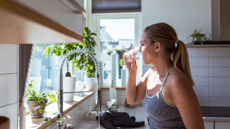 Eine Frau steht in der Küche und trinkt ein Glas Leitungswasser.