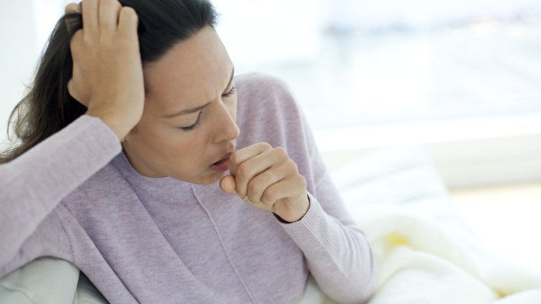 Atemwegserkrankungen: Eine Frau sitzt auf dem Sofa und hustet.