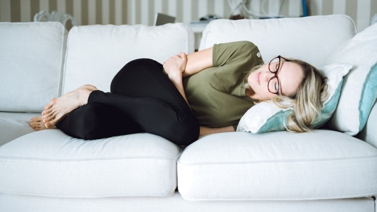 Eine Frau liegt mit Bauchschmerzen auf dem Sofa.
