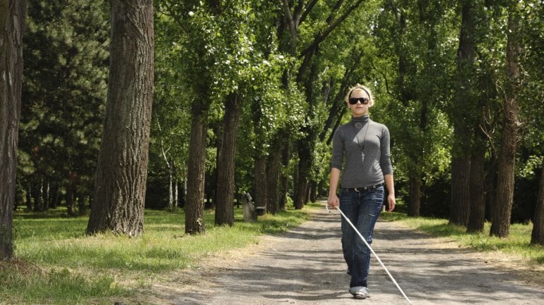 Eine blinde Frau läuft auf einem Parkweg.