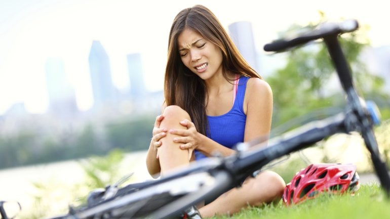 Eine Frau ist mit dem Fahrrad gestürzt und hält sich das schmerzende Bein.