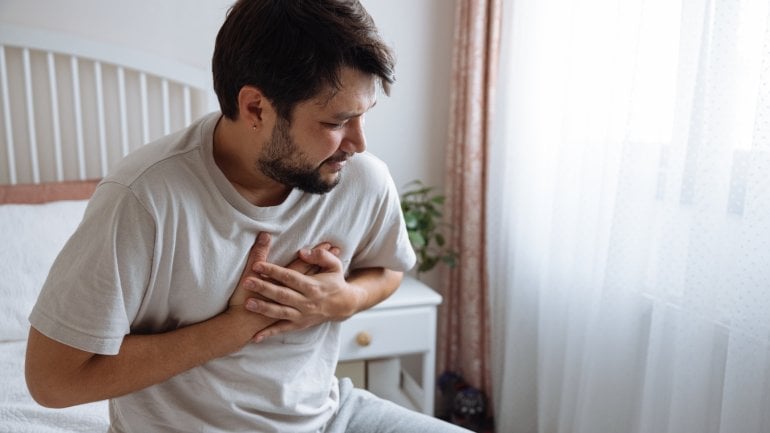 Mann mit Brugada-Syndrom leidet unter Herzrhythmusstörungen und sitzt auf dem Bett.