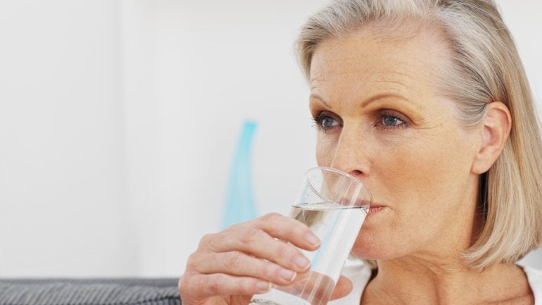 Eine ältere Frau trinkt aus einem Glas Wasser.