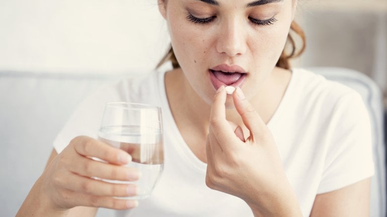 Eine junge Frau nimmt eine Tablette ein und hält ein Glas Wasser in der Hand.