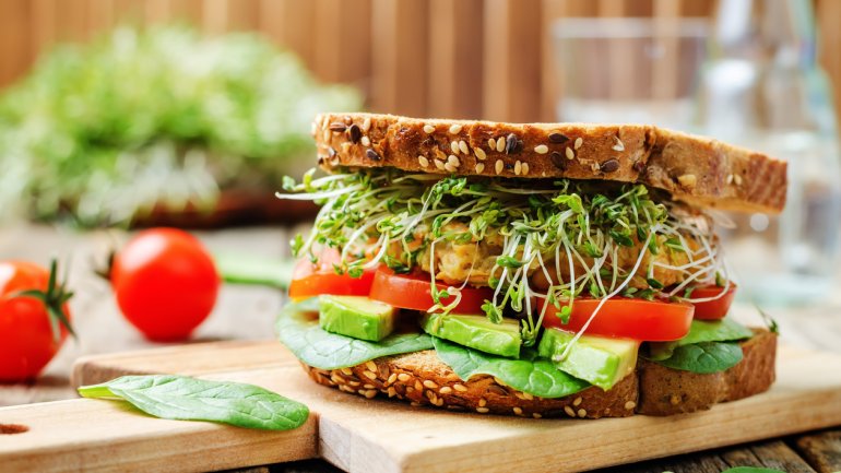 Man sieht ein Vollkorn-Sandwich mit Spinat, Avocado, Tomate, Kichererbsen und Kresse.