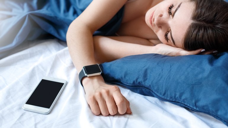 Eine Frau schläft neben ihrem Handy und trägt eine Smartwatch