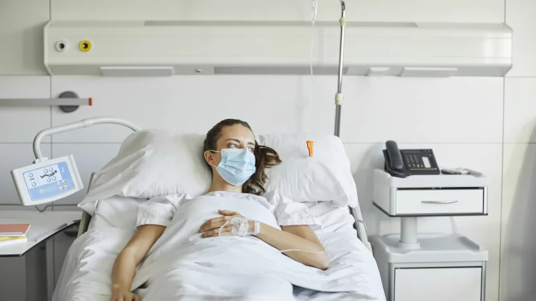 Eine junge Frau mit Mundschutz liegt im Krankenhausbett