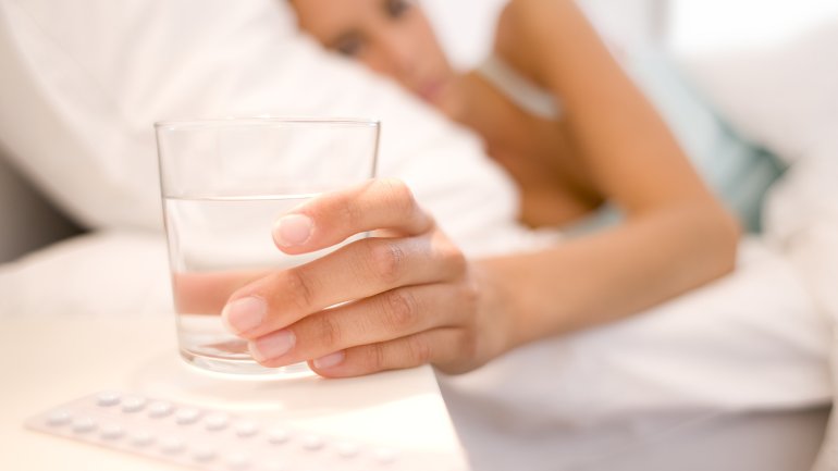 Eine im Bett liegende Frau greift nach einem Glas Wasser.