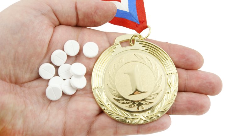 Das Bild zeigt eine Handfläche, in der Tabletten und eine goldene Medaille liegen.