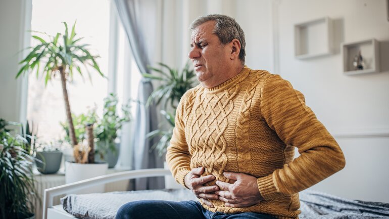 Dünndarmtumor: Ein älterer Mann sitzt auf dem Sofa und hat Bauchschmerzen