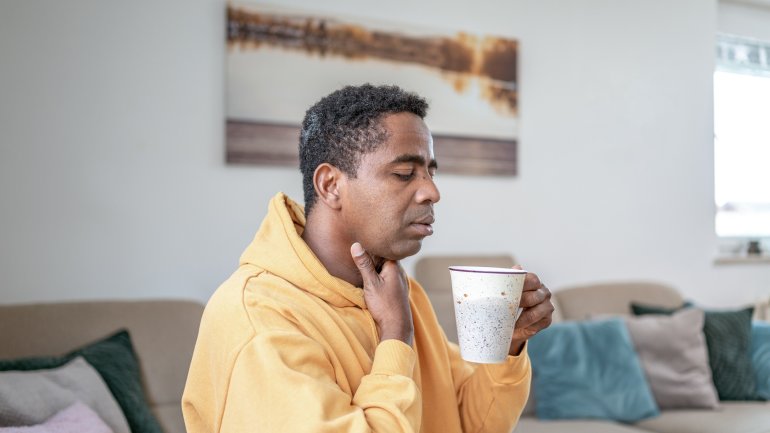 Dysphagie: Mann mit Schluckstörung fasst sich an schmerzenden Hals.