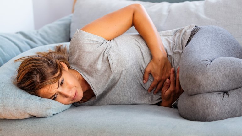 Frau mit Unterleibsschmerzen auf dem Sofa.