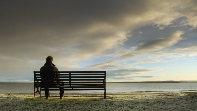 Die Rückansicht eines Mannes, der auf einer Bank am Meer sitzt.