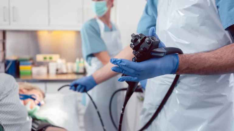 Eine Frau liegt auf einem OP-Tisch, ein Arzt hält ein Endoskop, eine Krankenschwester steht daneben