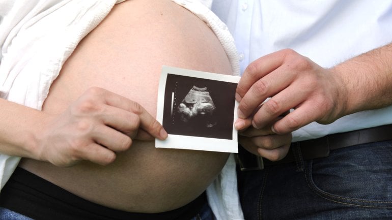 Das Bild zeigt eine Pärchen, das ein Ultraschallbild von ihrem Kind in den Händen hält.