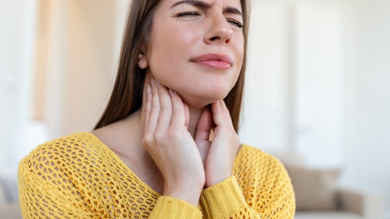 Frau mit Epiglottitis fasst sich an schmerzenden Hals.