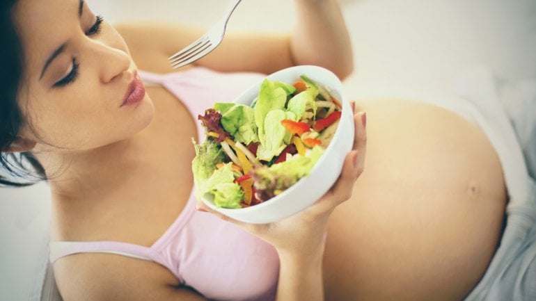 Schwangere Frau isst einen Salat.