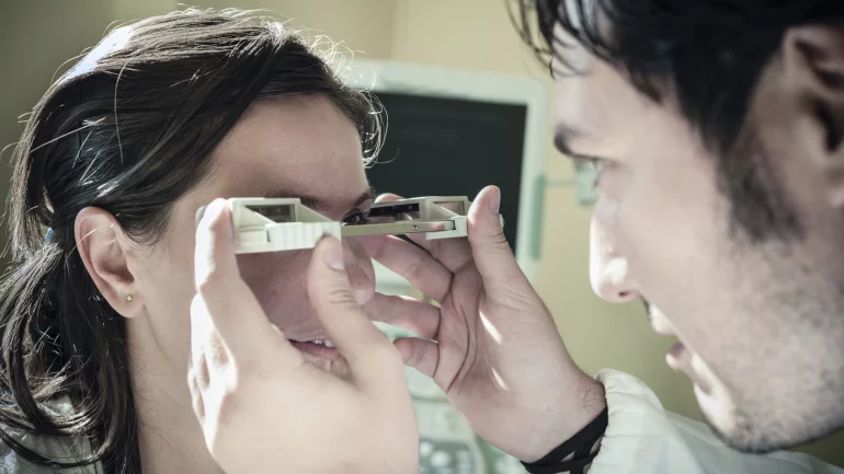 Eine Augenarzt untersucht die Augen einer Frau mit einem Exophthalmometer.