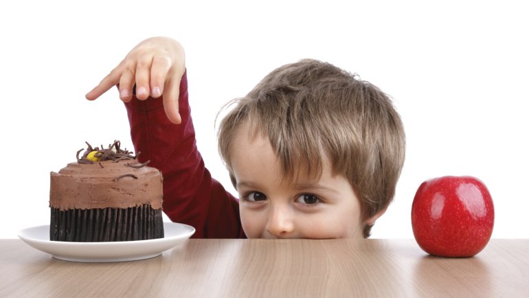 Das Bild zeigt einen kleinen Junge, der nach einem Stück Schokoladenkuchen greift. 