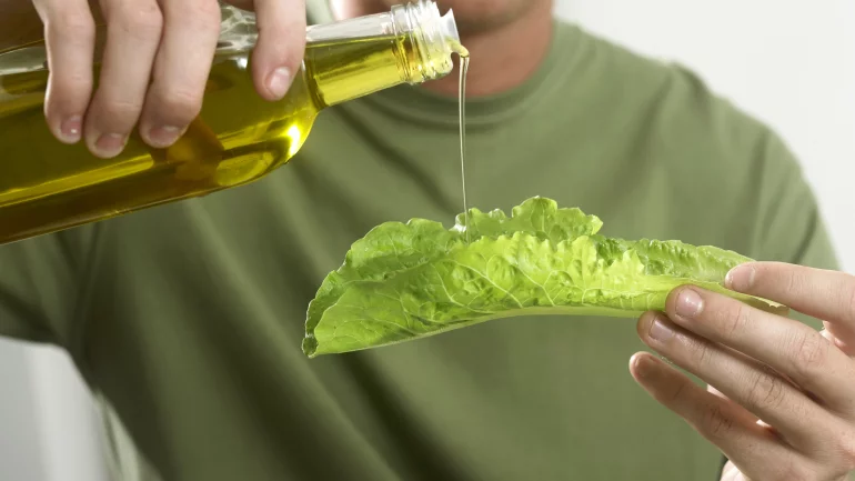 Das Bild zeigt einen Mann, der Öl auf ein Salatblatt gießt. 