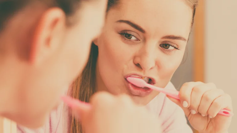 Eine Frau putzt sich vor einem Spiegel die Zähne.