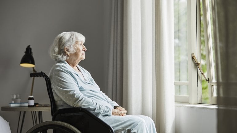 Eine alte Dame sitzt im Rollstuhl und schaut aus dem Fenster