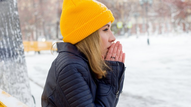 Eine frierende Frau sitzt im verschneiten Park auf einer Bank und wärmt ihre Hände.