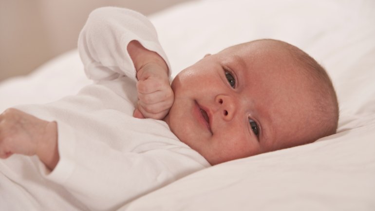 Das Bild zeigt ein Baby, das auf einem Bett liegt.