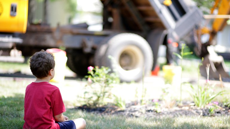 Ein kleiner Junge sitzt auf dem Rasen und beobachtet einen Bagger.