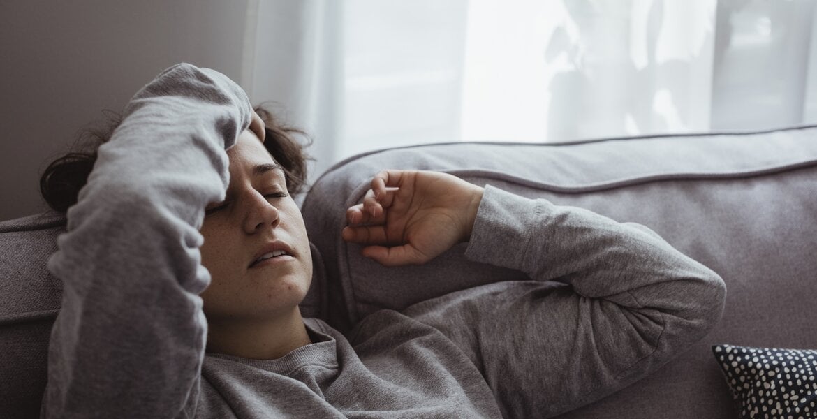 Eine Frau liegt mit Kopfschmerzen auf dem Sofa