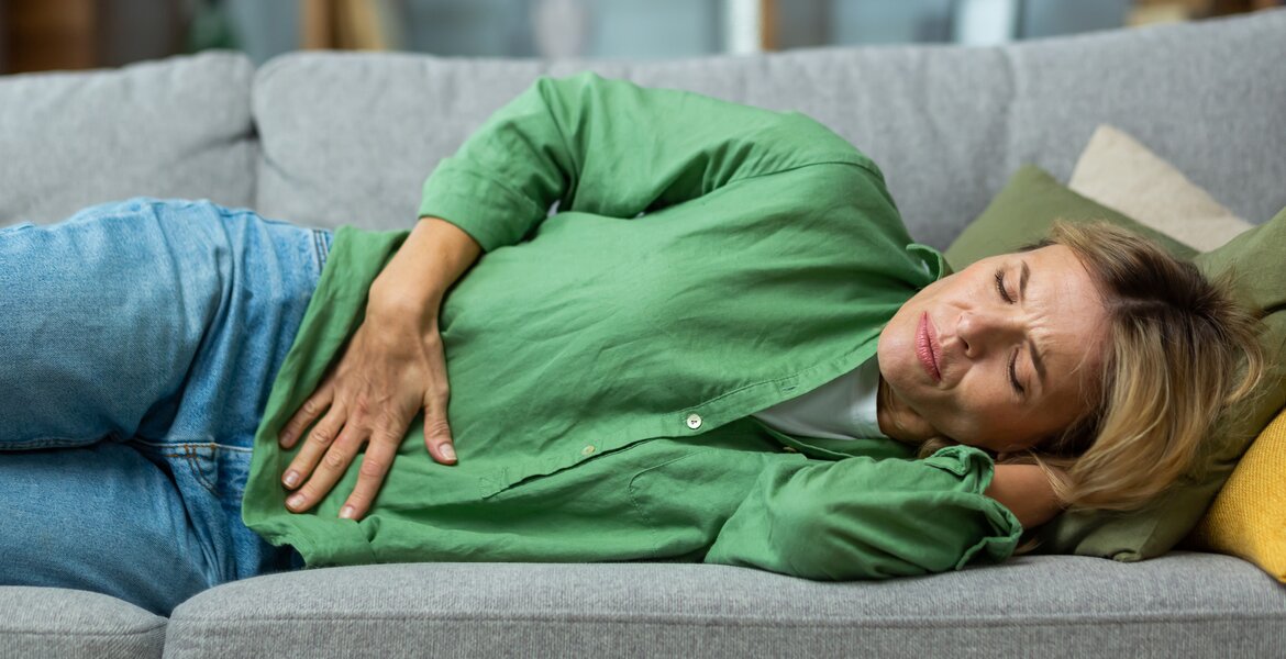 Frau mit Colitis ulcerosa liegt auf dem Sofa und leidet unter dem Symptom Bauchschmerzen.