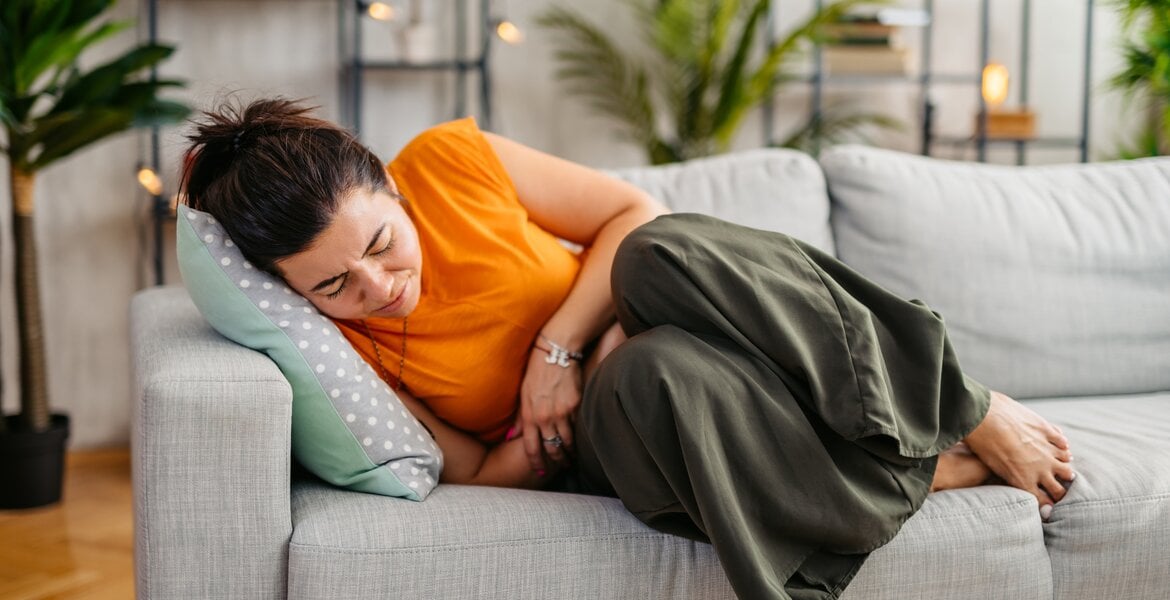 Frau mit Endometriose liegt auf dem Sofa und hat Magen-Darm-Symptome wie Blähungen.