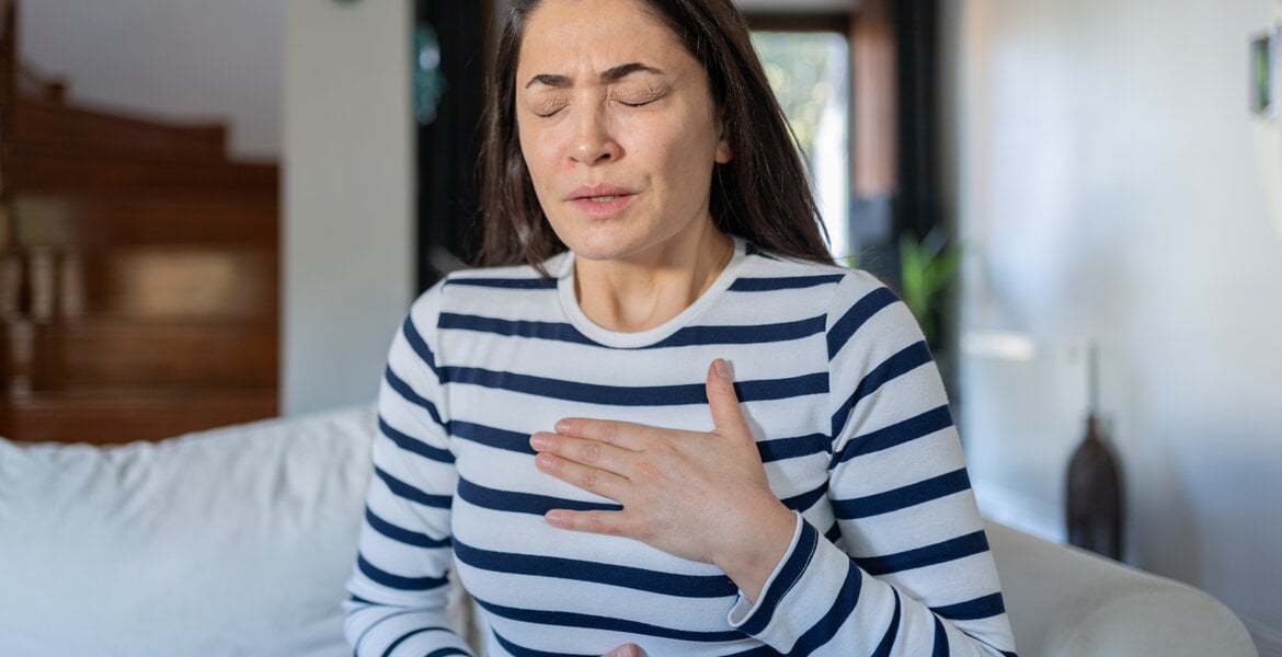 Eine Frau hat Herzrasen, während sie auf dem Sofa sitzt