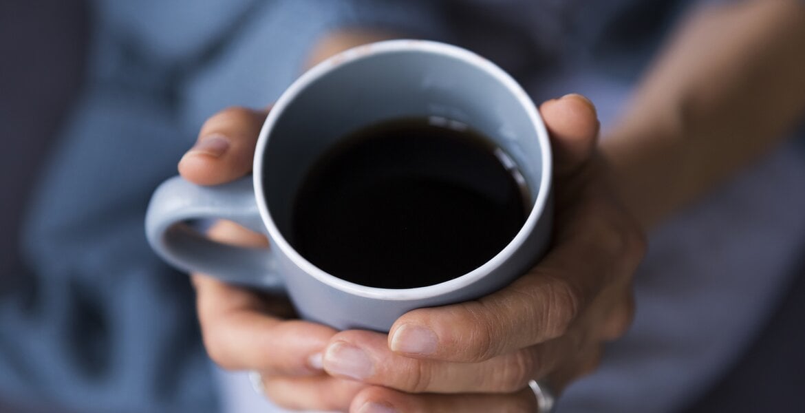 Leber reinigen Lebensmittel: Eine Frau hält eine Tasse schwarzen Kaffee in der Hand