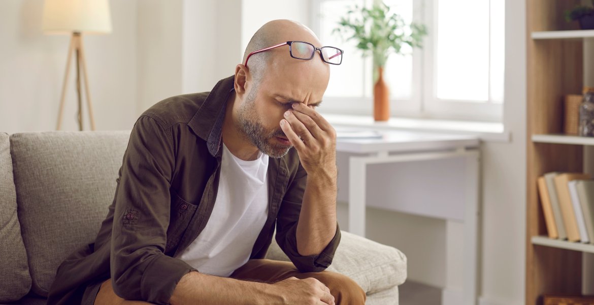 Mann mit Leberkrebs sitzt auf Sofa und leidet unter unspezifischen Symptomen wie Müdigkeit.