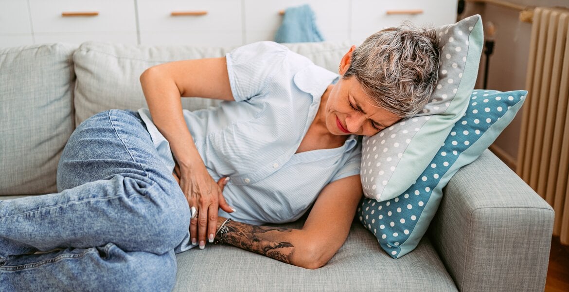 Magendurchbruch: Eine Frau liegt auf dem Sofa und hat Magenschmerzen