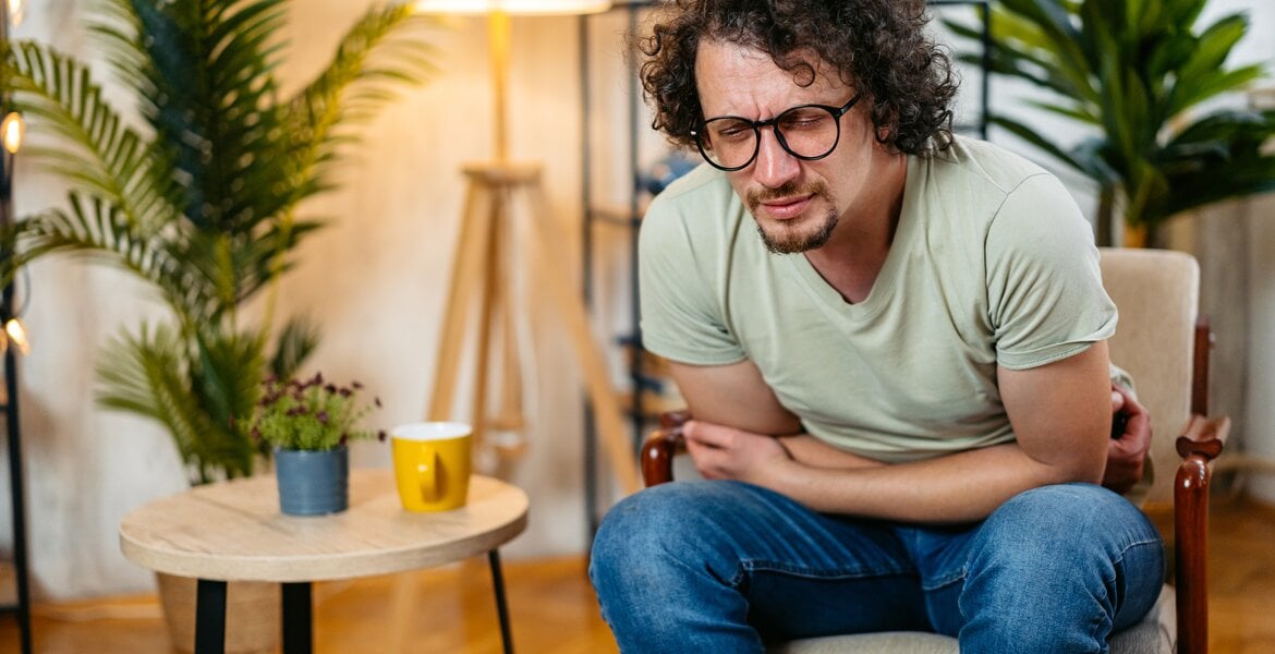 Magenkrebs Metastasen: Ein Mann mittleren Alters zuhause auf einem Sessel beugt sich vor wegen Magenschmerzen