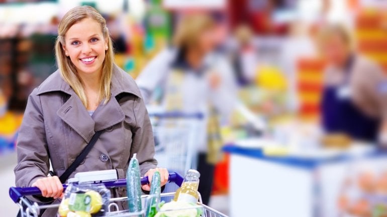 Eine Frau im Supermarkt schiebt ihren gefüllten Einkaufswagen
