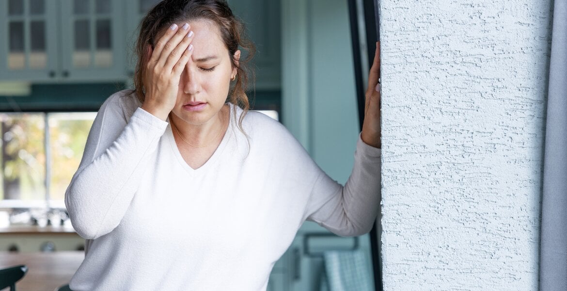 Eine Frau fasst sich an den Kopf, ihre Augen hat sie geschlossen