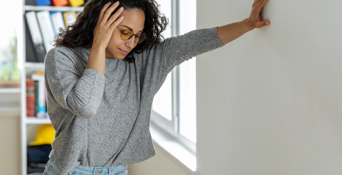 Schleichender Schlaganfall: Eine junge Frau lehnt an einer Wand zuhause