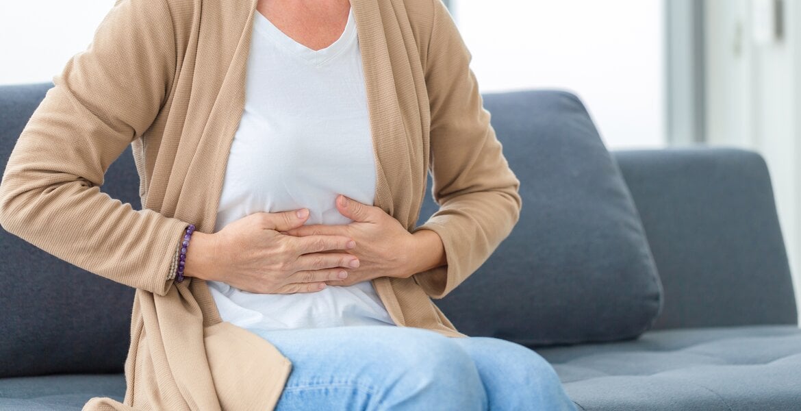 Frau mit Gallensteine fasst sich an den Oberbauch und sitzt auf dem Sofa.