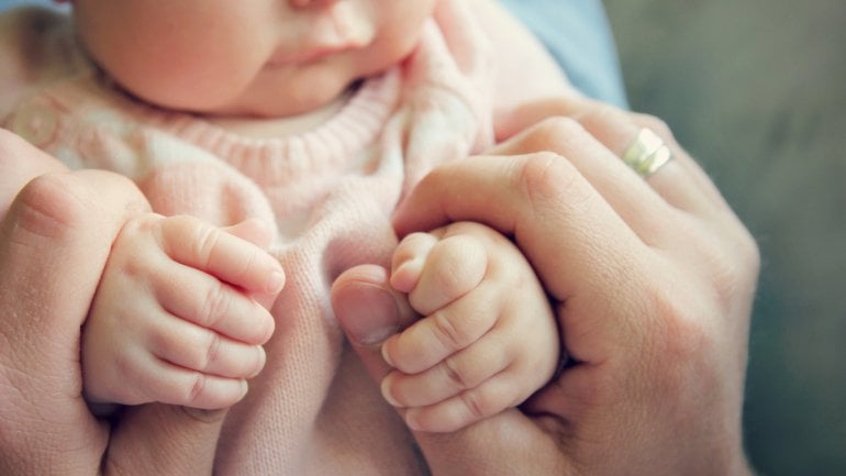 Jemand umfasst die Hände eines Babys.