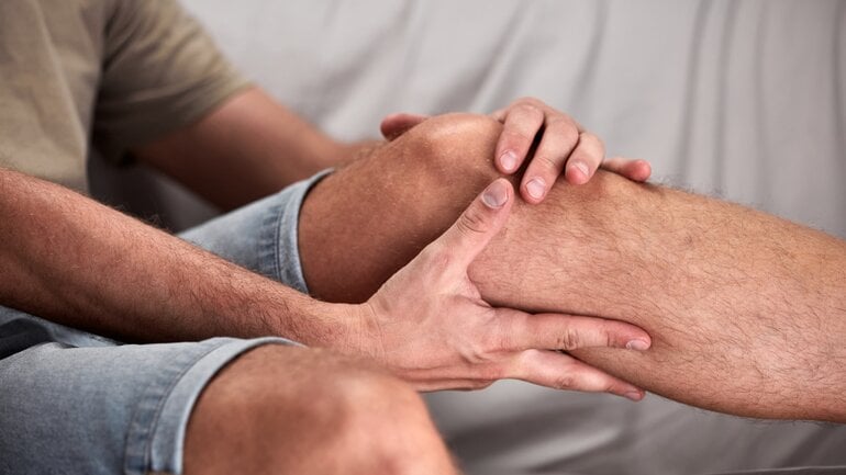 Ein mann mit Knieschmerzen greift sich mit beiden Händen an das Knie. 