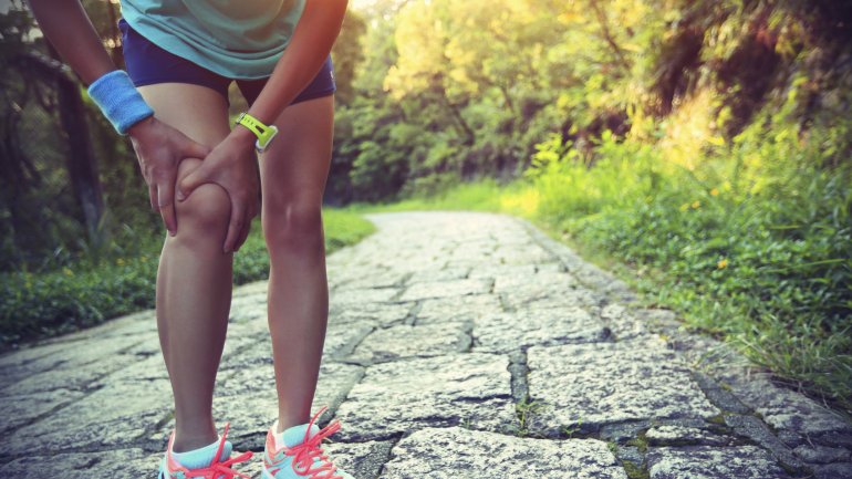 Das Bild zeigt eine Läuferin, die vor Schmerzen ihr Knie hält.