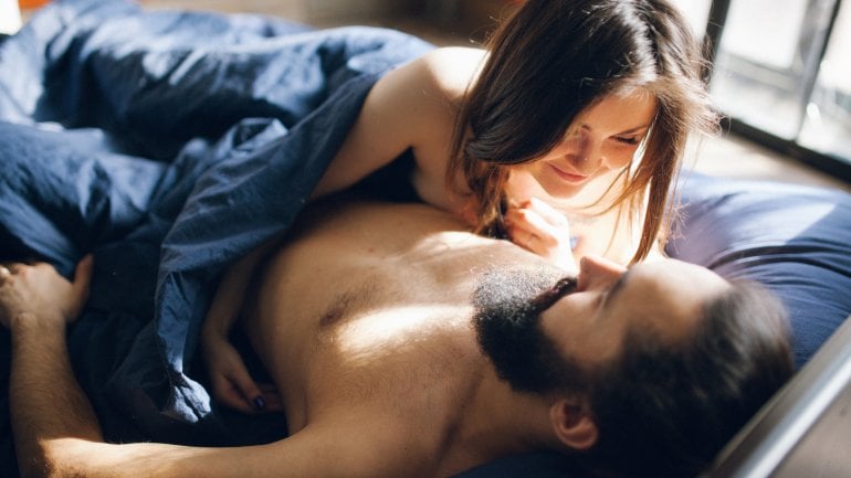 Geschlechtsverkehr: Junges Pärchen liegt in zärtlicher Pose im Bett