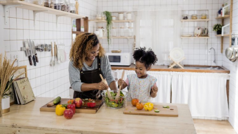 Eine Mutter steht gemeinsam mit ihrer kleinen Tochter in der Küche und macht einen Salat