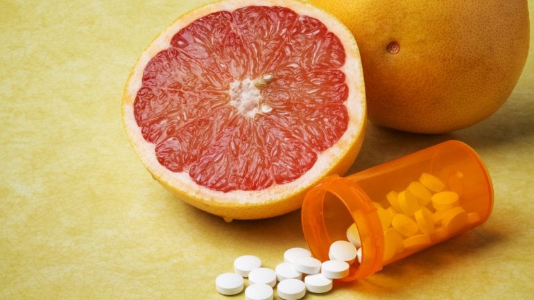 Man sieht eine aufgeschnittene Grapefruit neben einem Döschen mit Tabletten
