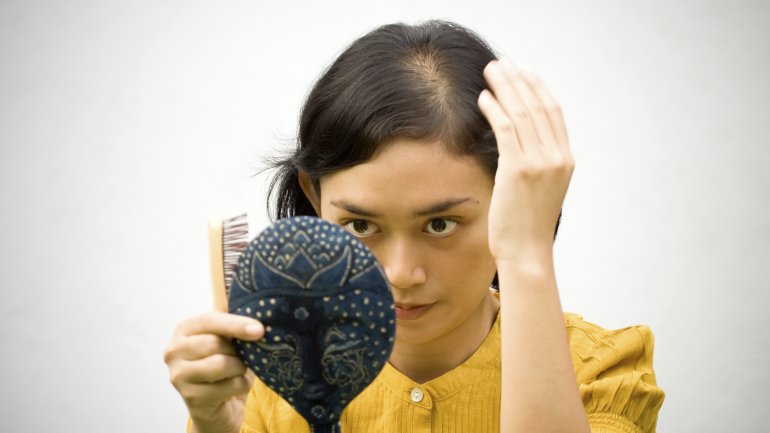 Frau mit Haarausfall betrachtet ihren Scheitel.