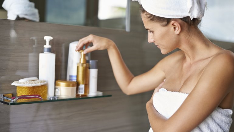 Eine Frau schaut sich Kosmetikprodukte in einem Badezimmer an. 
